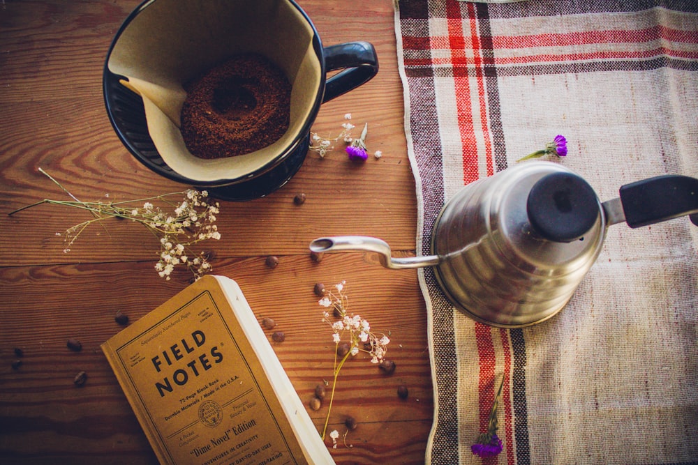 Libro de notas de campo cerca de la taza de café y la tetera