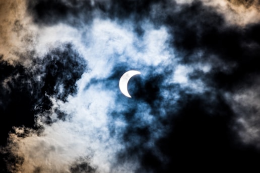 A partially covered sun creates a solar eclipse effect, surrounded by swirling clouds with a mix of bright and dark areas.