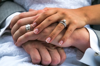 Close-up of intertwined hands wearing matching vintage-inspired rings, set against a soft beige fabric.