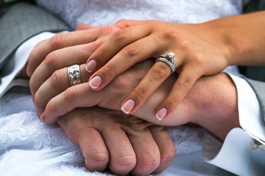 A close-up of intertwined hands with wedding rings, resting on an open Bible.