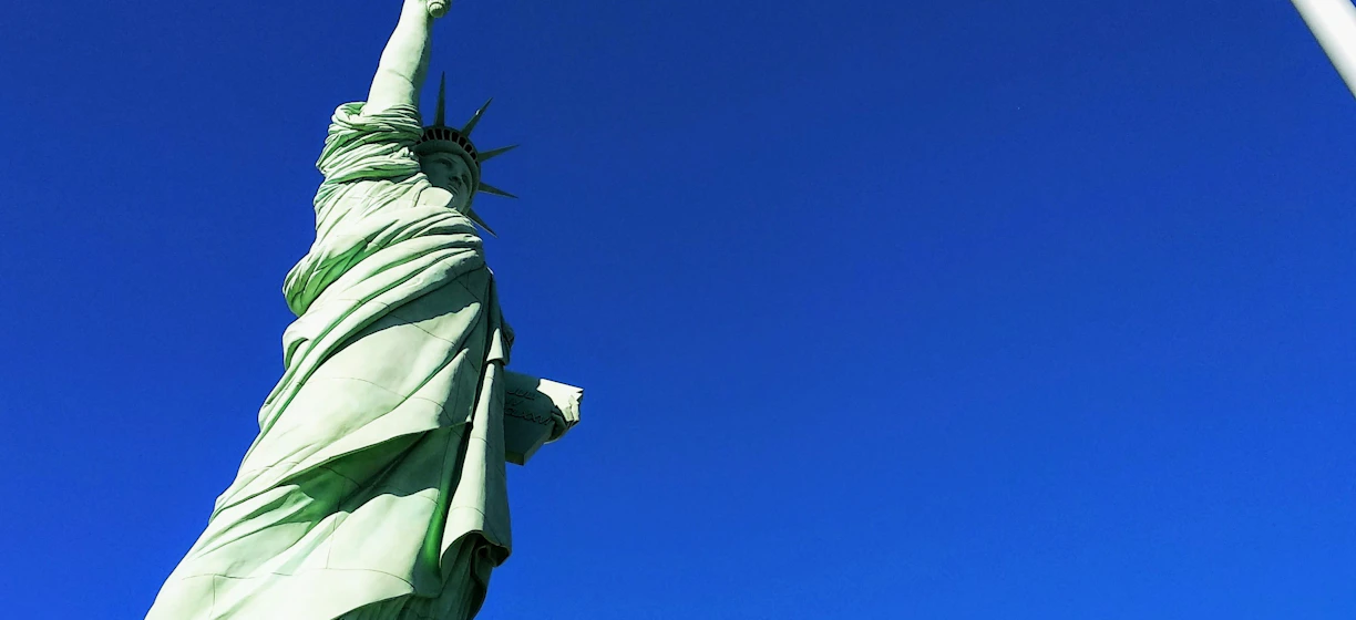 Statue of Liberty in front USA flag under blue sky