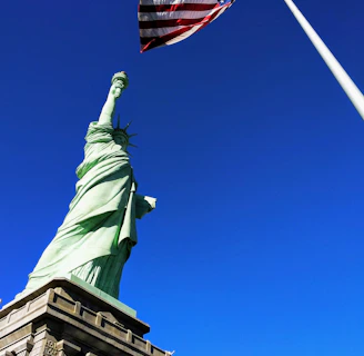 Statue of Liberty in front USA flag under blue sky