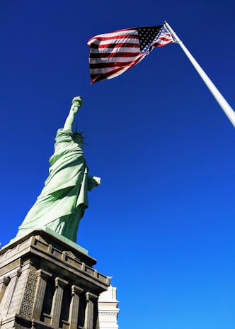 Statue of Liberty in front USA flag under blue sky