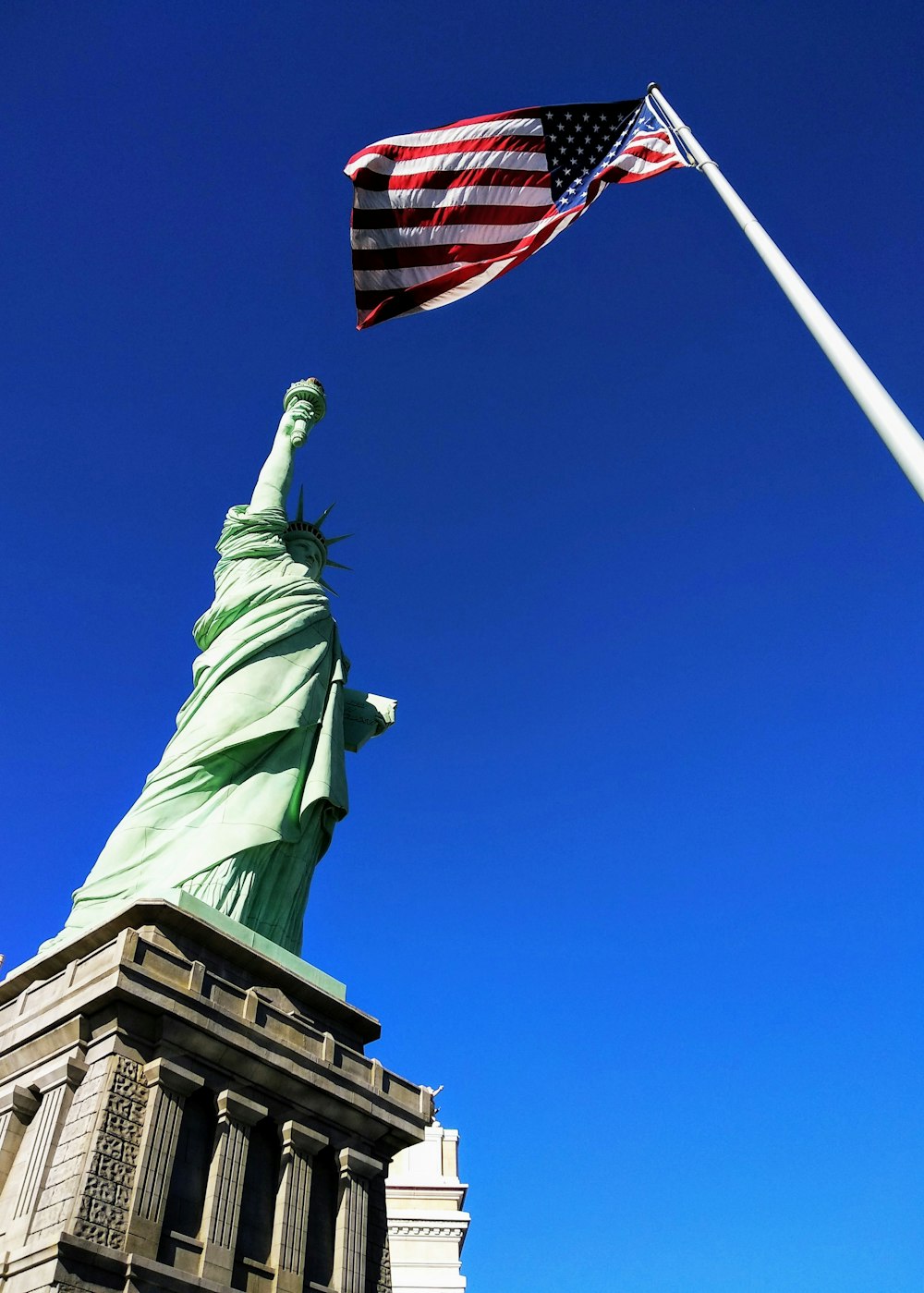 Statue of Liberty in front USA flag under blue sky