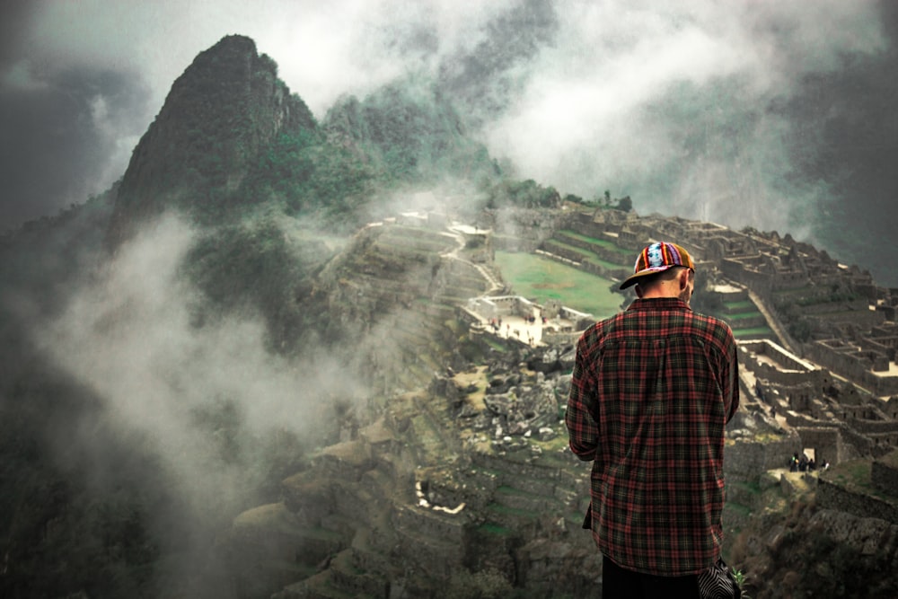 man standing on cliff facing mountain rice terraces