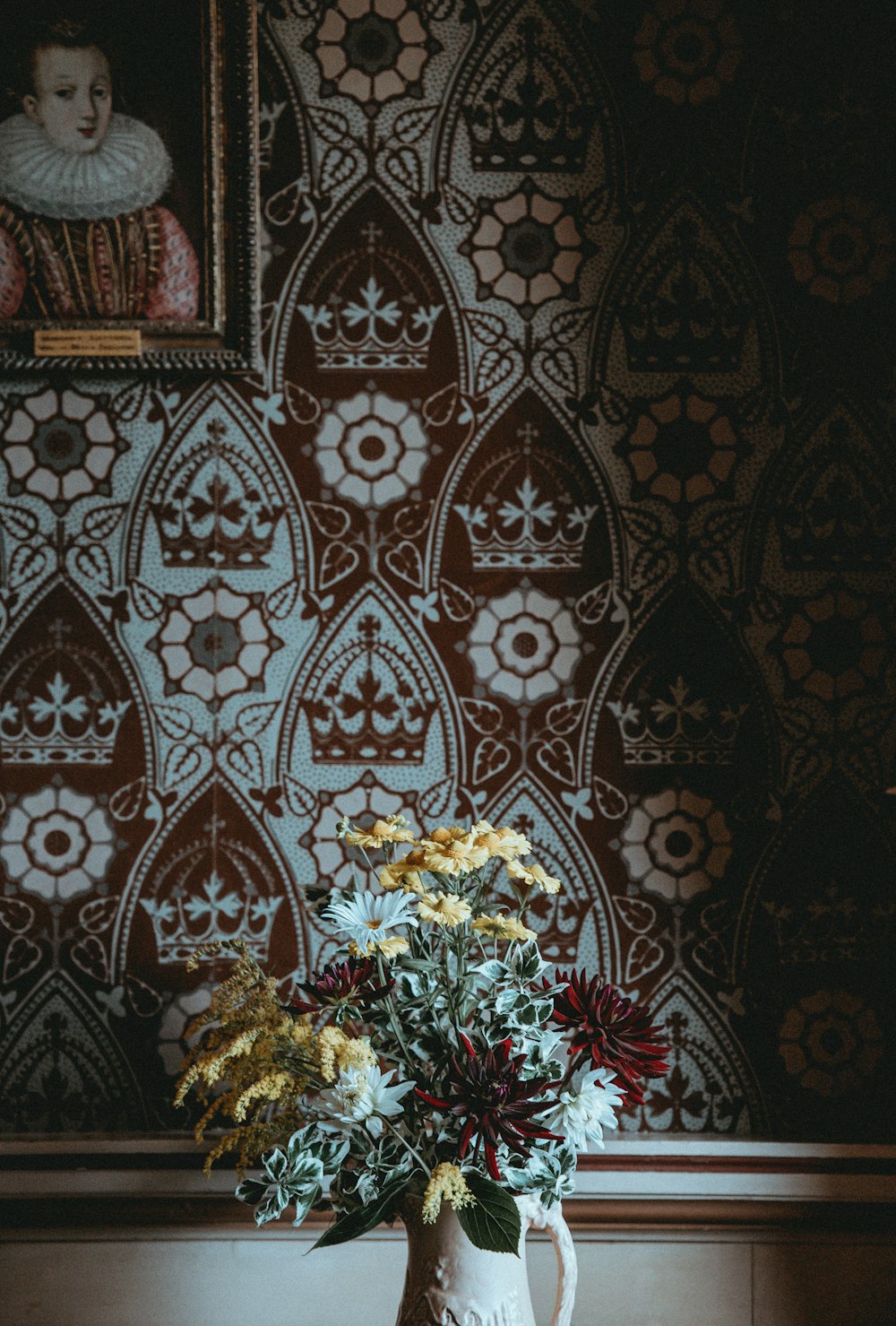 yellow, red, and white flowers in vase beside wall