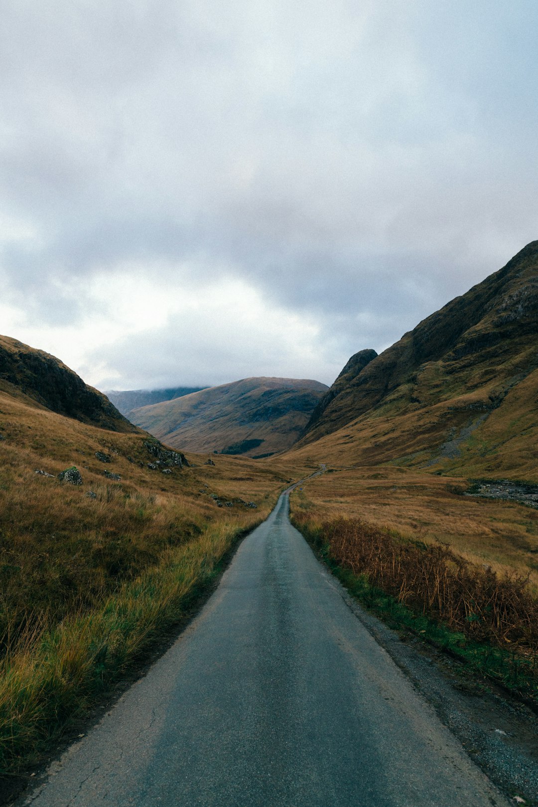 empty road between brown mountains under blue sky