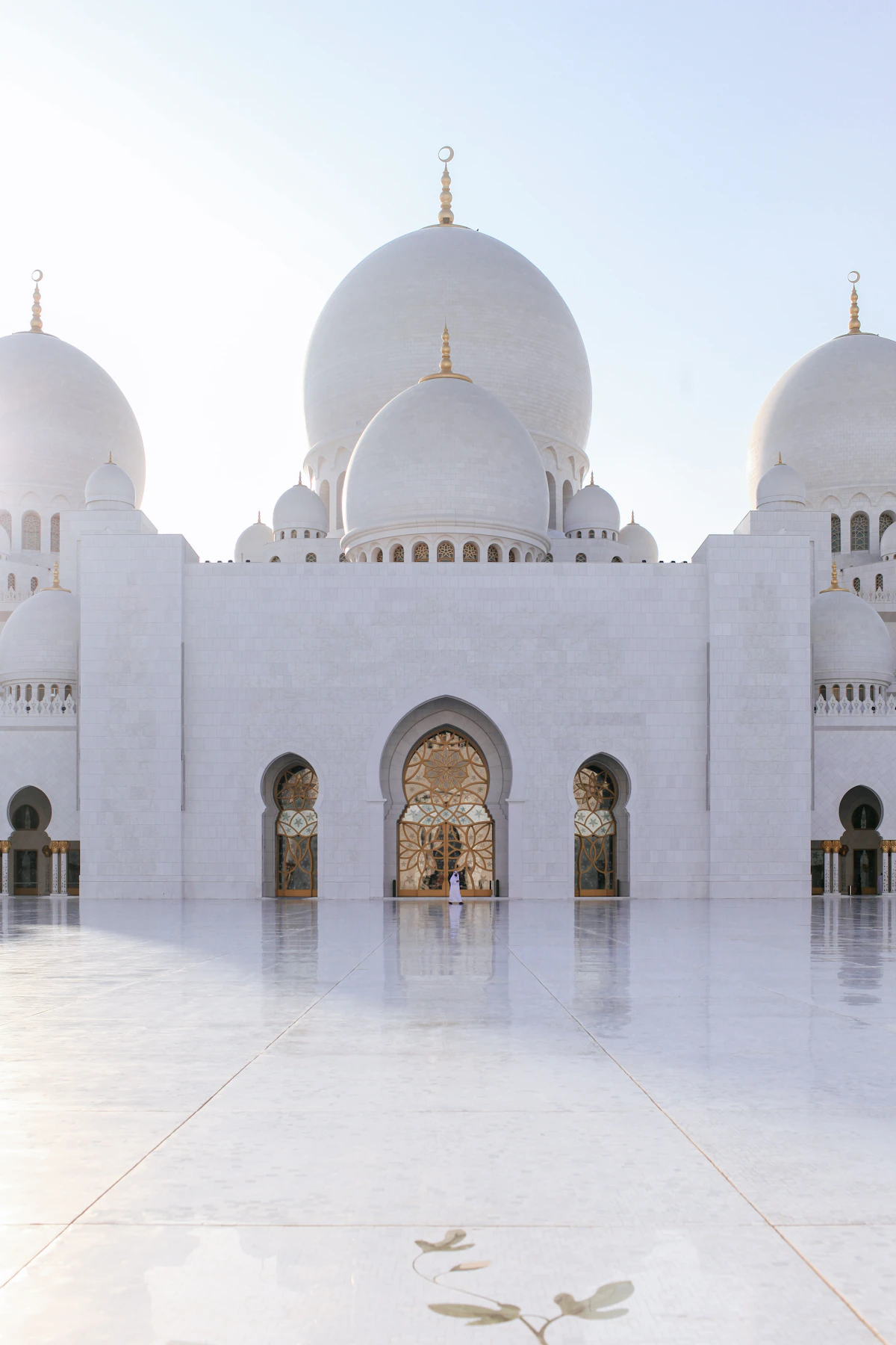 White domes and arched doorways of the Sheikh Zayed Grand Mosque in Abu Dhabi at golden hour