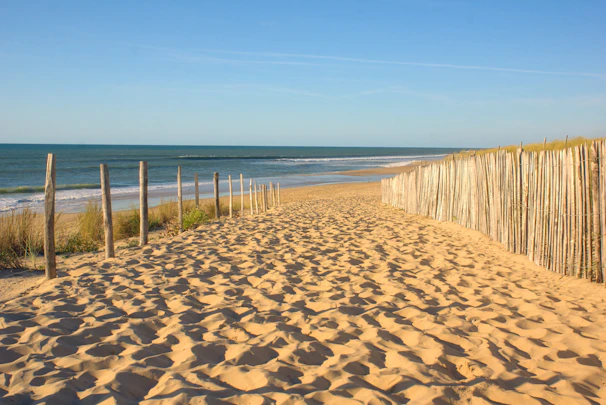 View of a sandy beach path leading from a charming house to the sea under a clear blue sky.