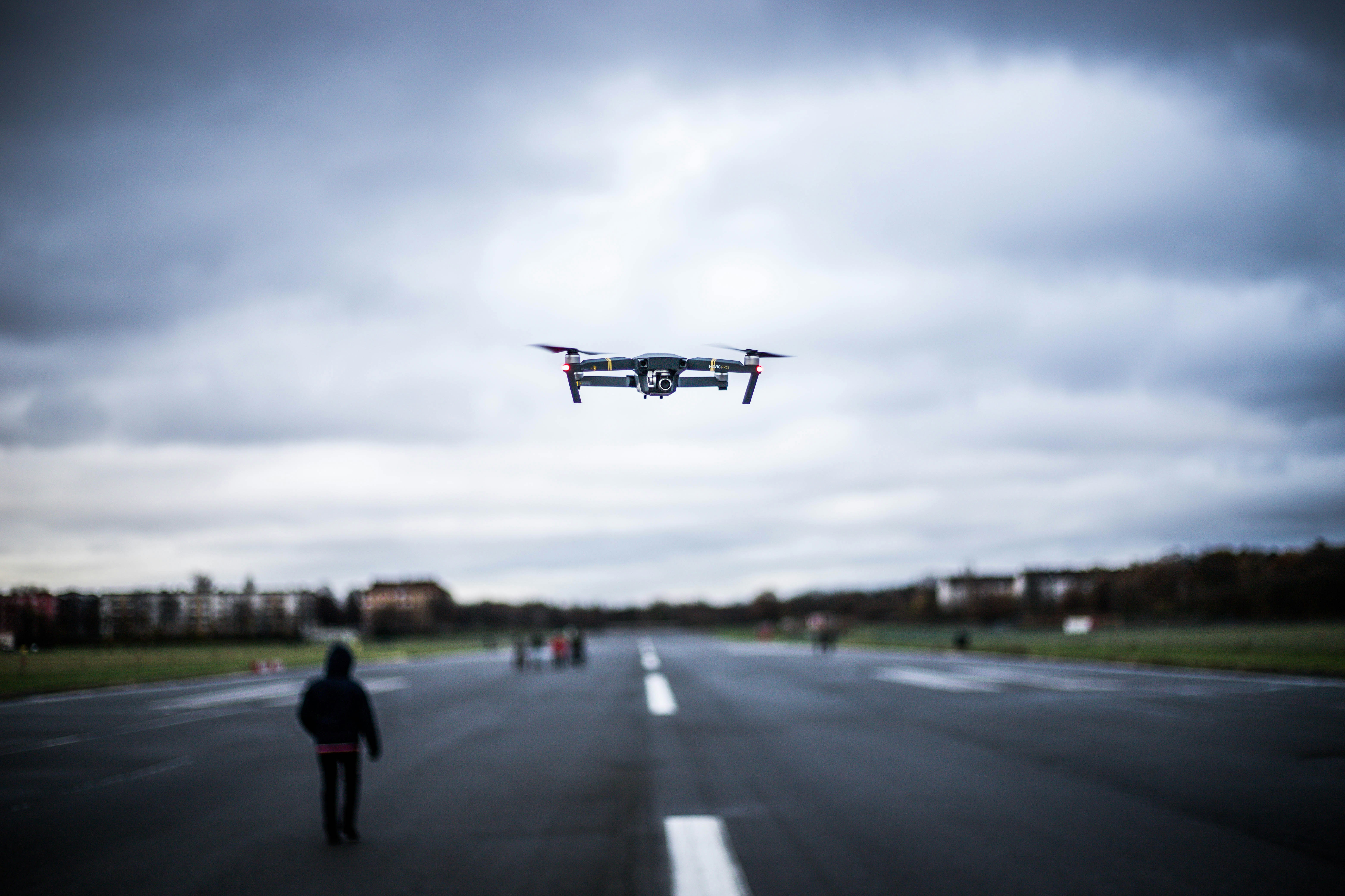 Drone hovering over an airport runway representing flight disruptions due to unidentified drones.