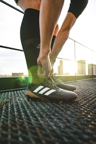 Close-up of a player tying black and red soccer cleats before training under stadium lights.