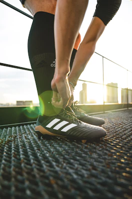 Close-up of a male athlete tying his cleats on a sunlit stadium field.