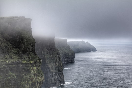 body of water surrounded by rock mountain during daytime in Cliffs of Moher Ireland