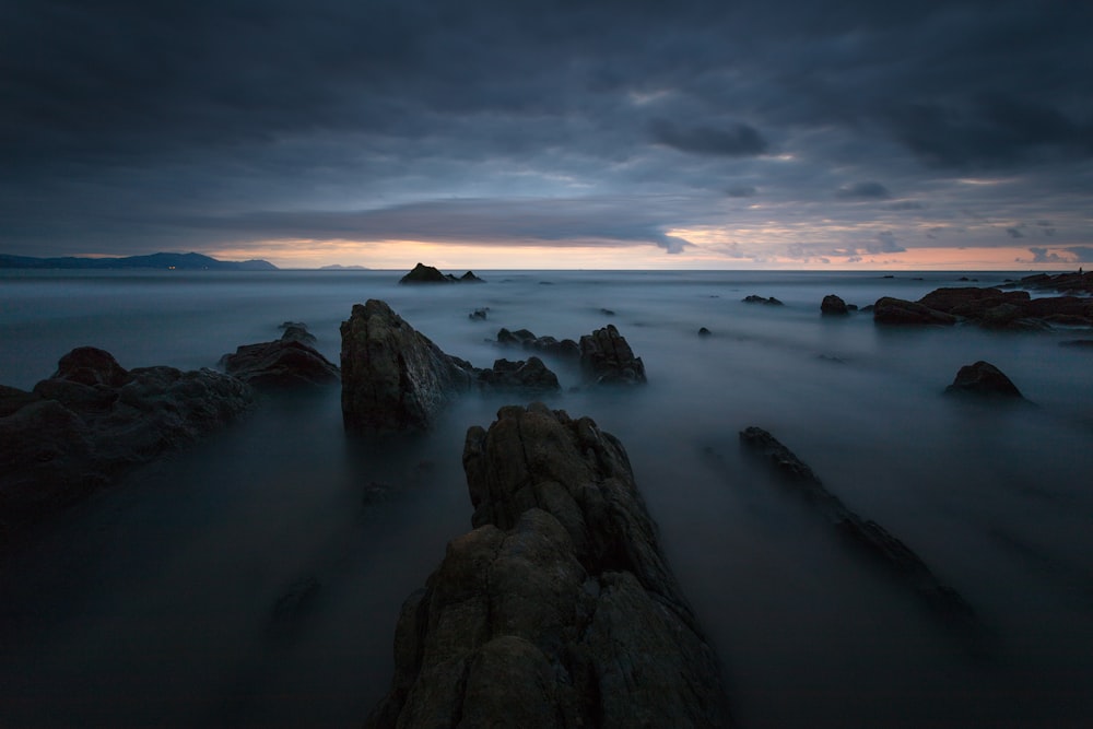 rock formations on body of water under cloudy sky