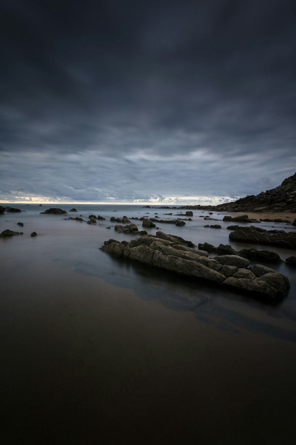 black rock formation on calm body of water under gray clouds