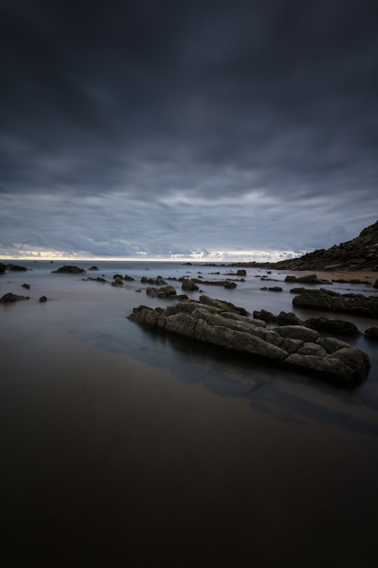 black rock formation on calm body of water under gray clouds in Barrika Spain
