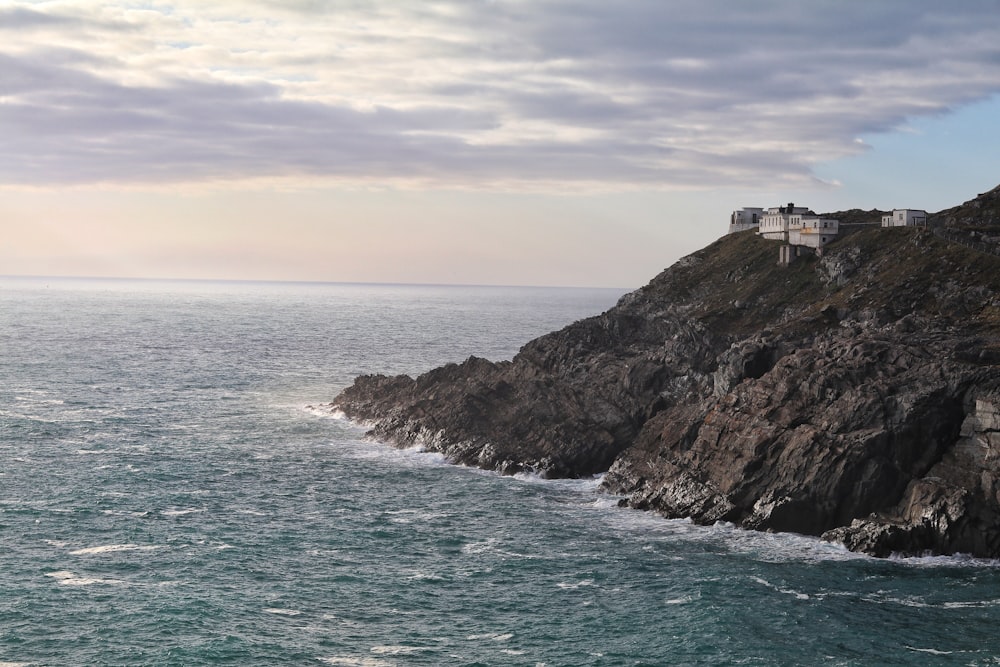 white house on cliff near body of water under cloudy sky at daytime