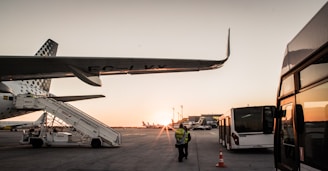 A busy airport tarmac with ground crew assisting an airplane during sunset.