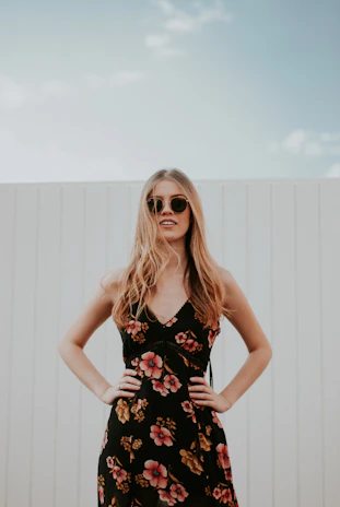 A confident plus-size woman wearing a vibrant floral dress, smiling outdoors on a sunny day.