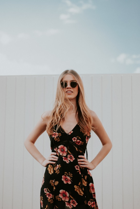 woman wearing black sunglasses standing near white wooden wall