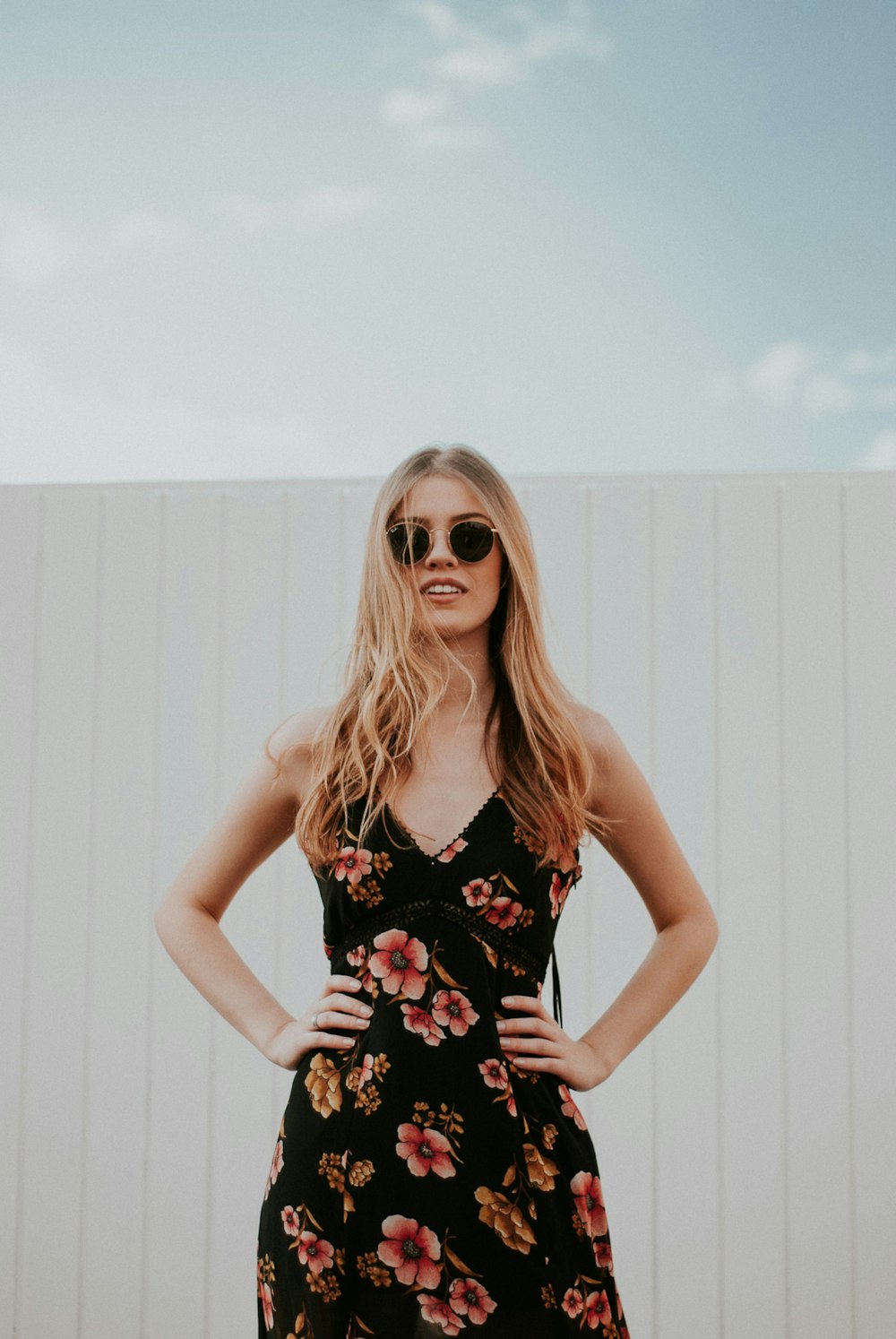 woman wearing black sunglasses standing near white wooden wall