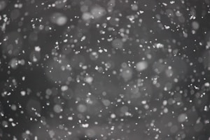 Snowflakes falling in a blurred field of view against a dark background, creating a serene and wintery atmosphere.