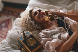 woman laying on white bed using a brown telephone