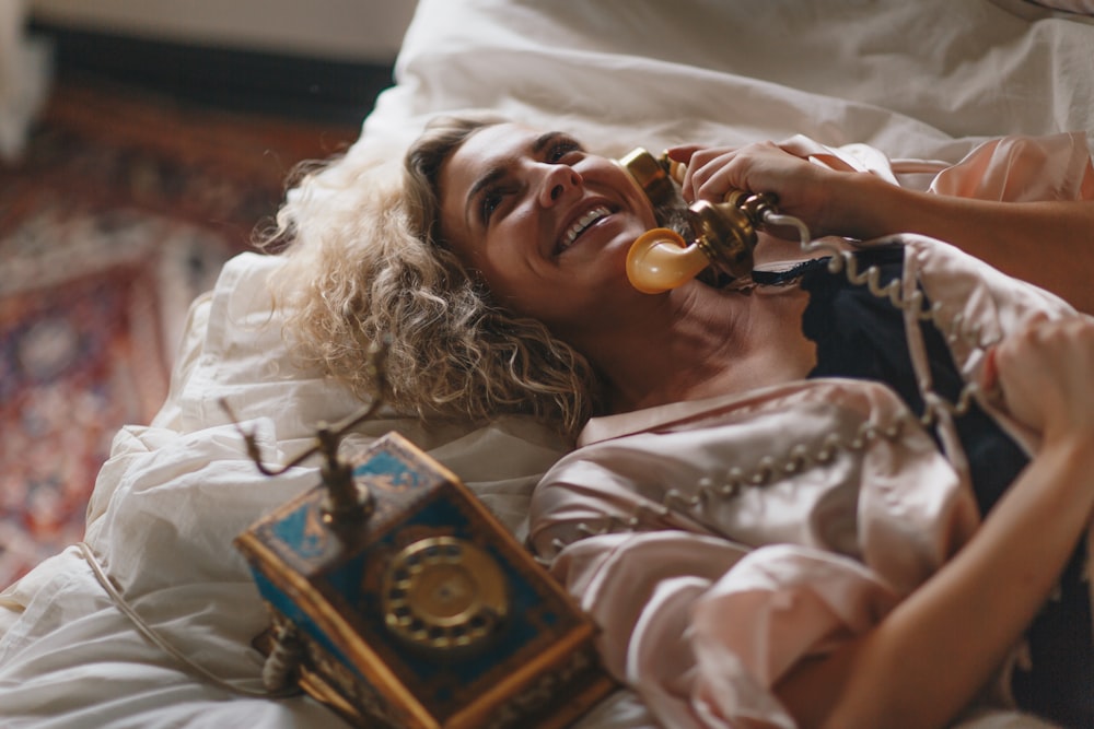 woman laying on white bed using a brown telephone