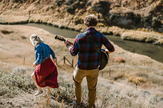 man playing guitar standing behind woman on mountain