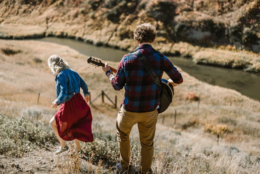 man playing guitar standing behind woman on mountain