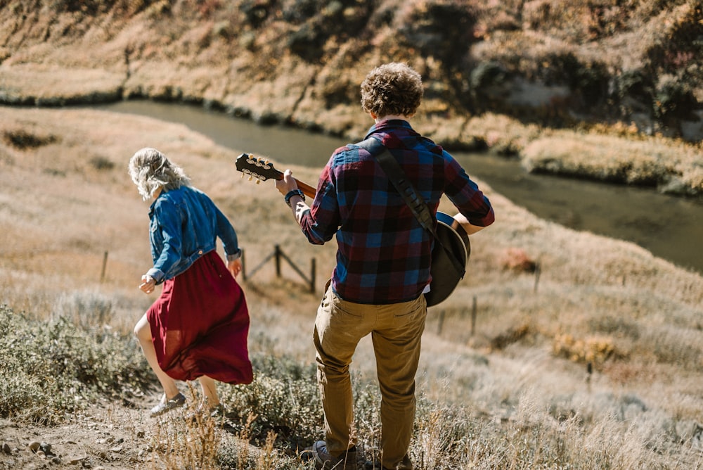 man playing guitar standing behind woman on mountain