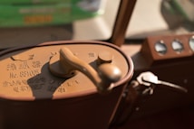 A close-up view of a vintage machine control panel with a large handle and various dials. The control panel has Chinese characters and a serial number imprinted on it, with a curved metallic lever visible beside it. The background is out of focus, revealing a mix of green and beige colors.