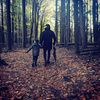 A family walking hand in hand through a sunlit forest in autumn.