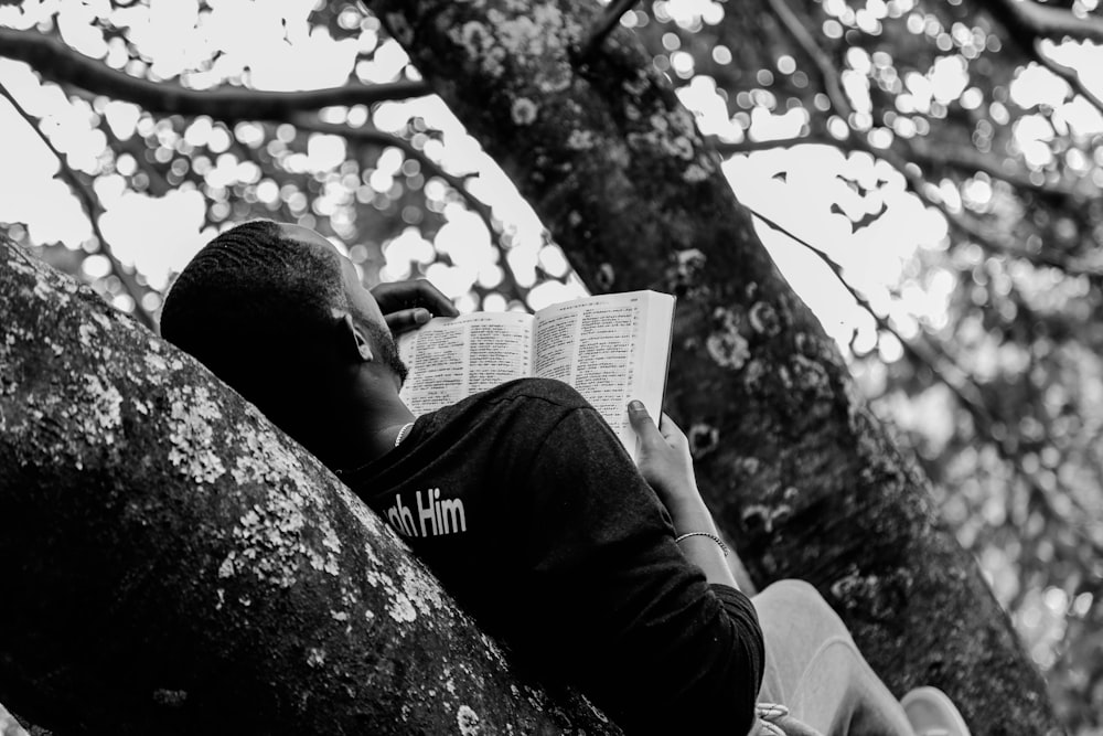 homme couché sur une branche tout en lisant un livre
