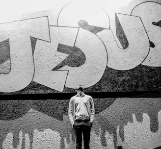 grayscale photography of a man standing in front of a Jesus graffiti