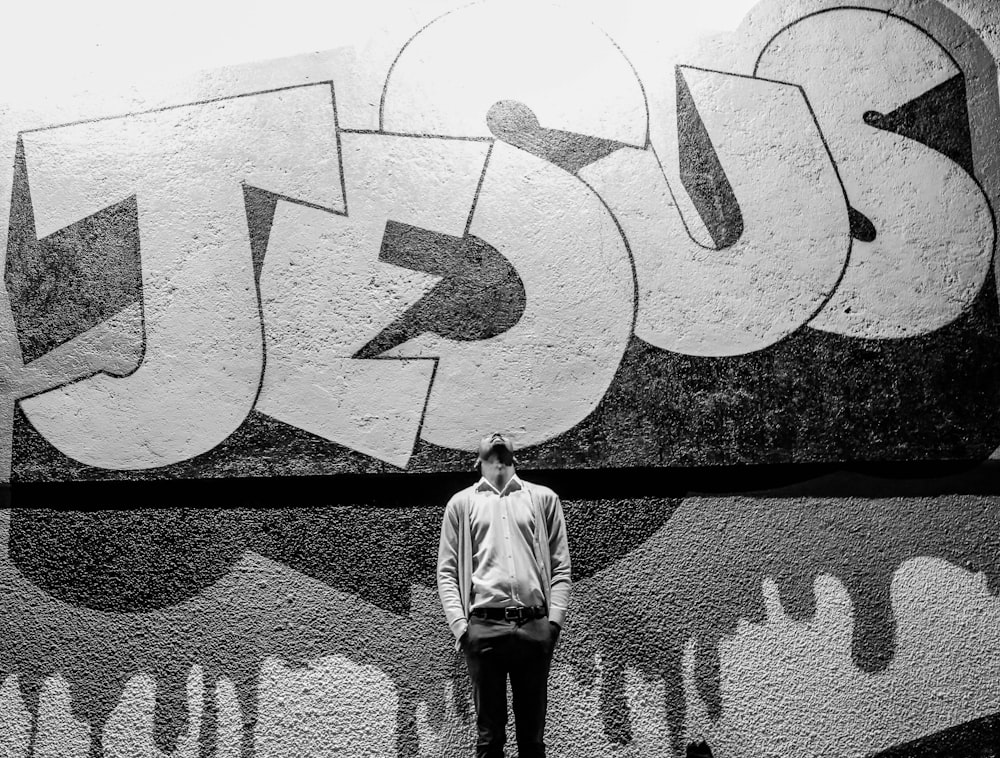 grayscale photography of a man standing in front of a Jesus graffiti