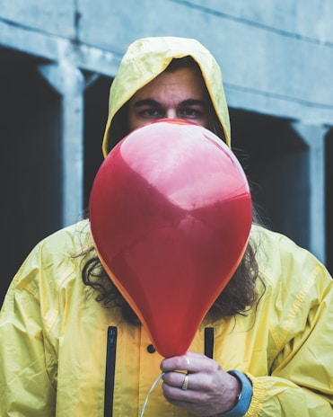 person on raincoat holding red balloon