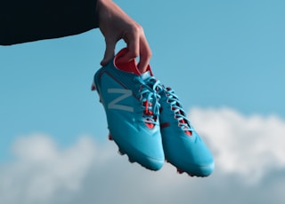 person holding pair of blue New Balance cleats