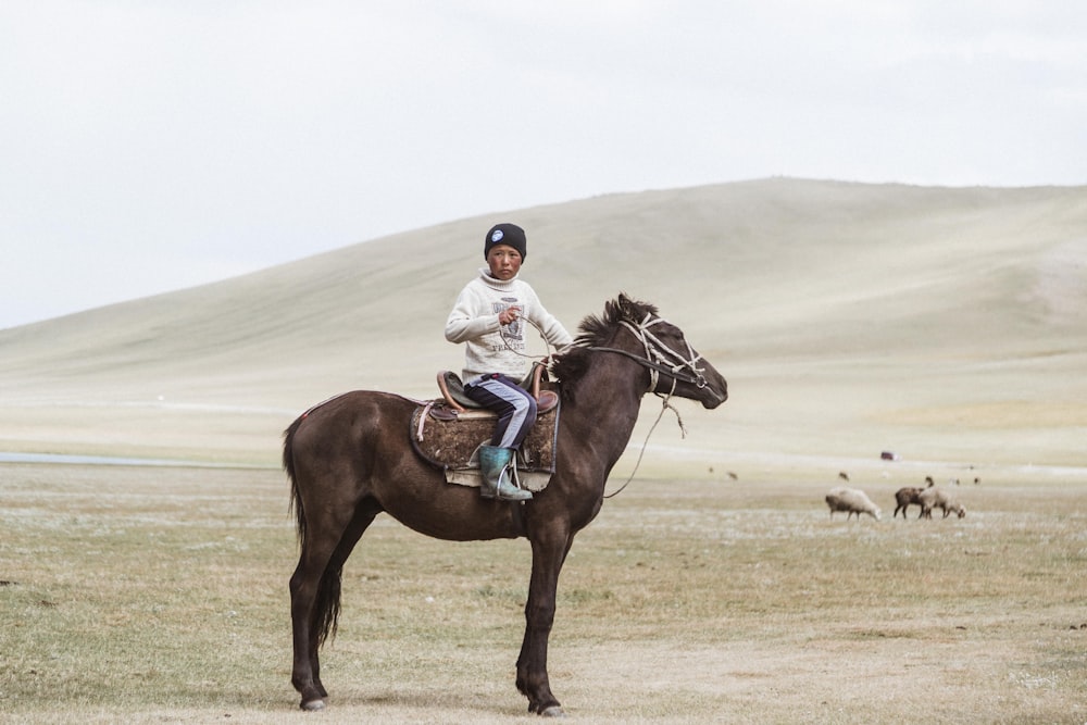 garçon en veste blanche chevauchant un cheval brun