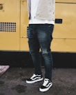 man wearing distressed black denim fitted jeans and pair of black Vans Old Skool shoes