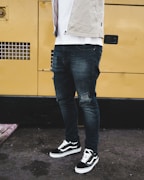 man wearing distressed black denim fitted jeans and pair of black Vans Old Skool shoes