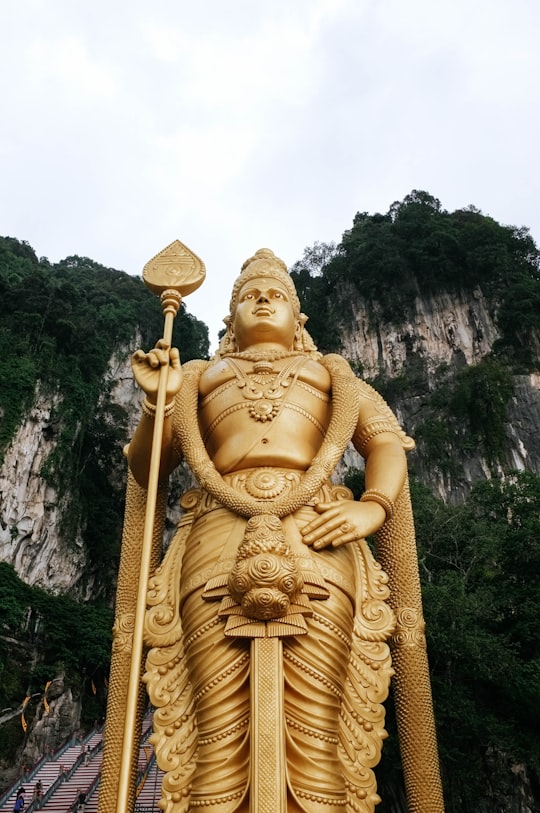 low angle photograph of Lord Murugan state near mountain cliff under cloudy sky in Batu Caves Malaysia