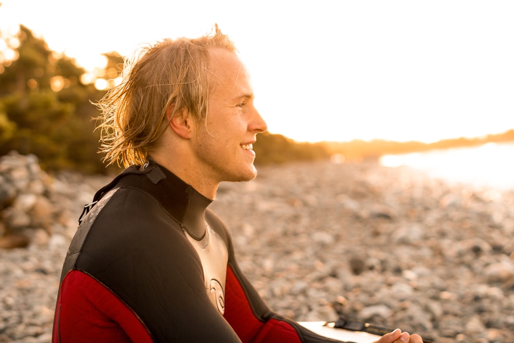 uomo sorridente che indossa la muta di fronte alla spiaggia