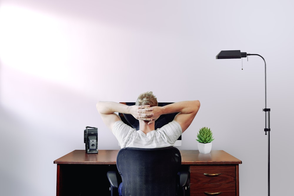 Mann hält seinen Kopf, während er auf einem Stuhl in der Nähe des Computertisches sitzt