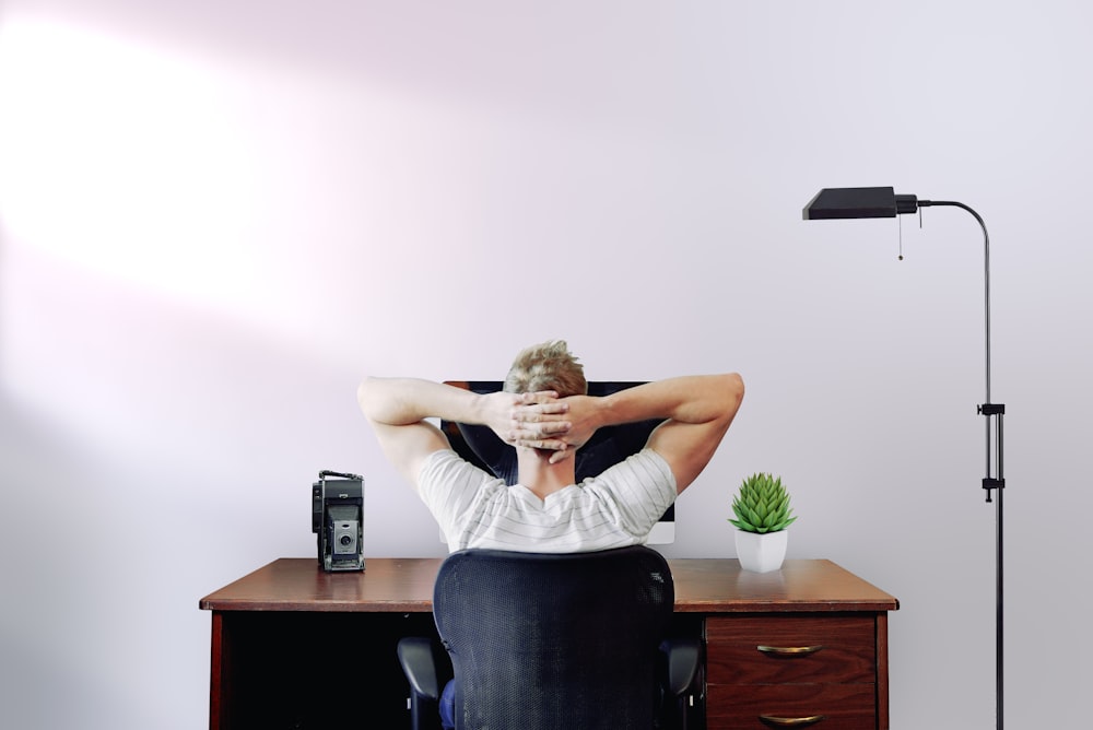 man holding his head while sitting on chair near computer desk