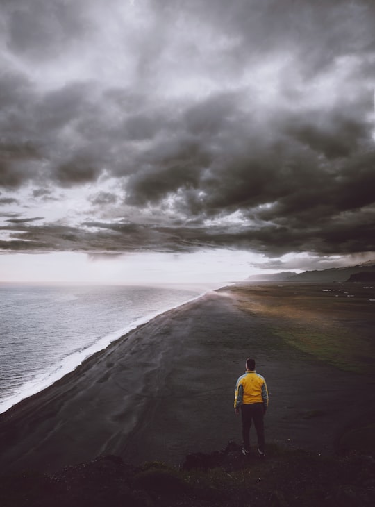 man standing on coastline under cloudy sky in Dyrhólaey Lighthouse Iceland