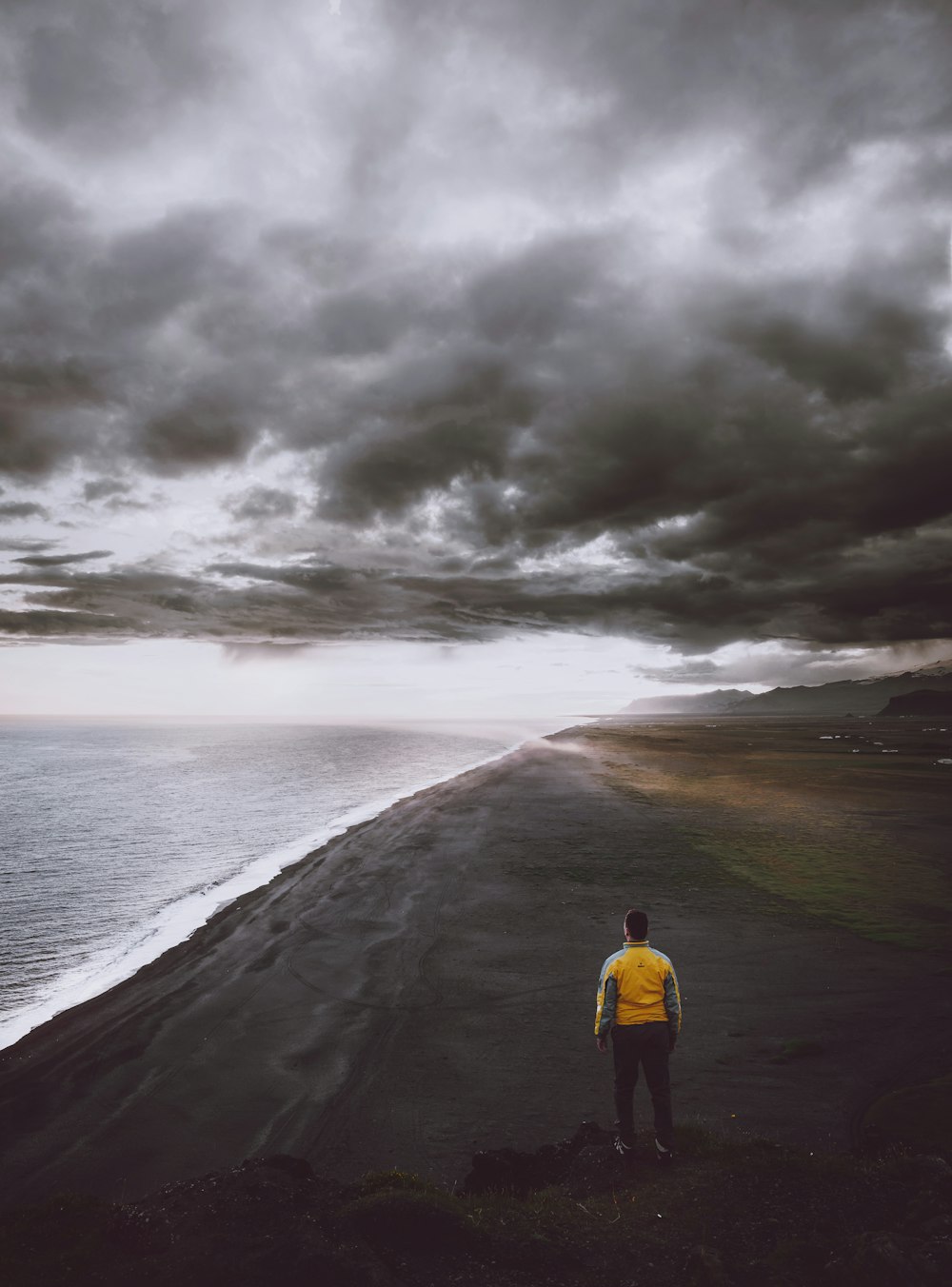 曇り空の下、海岸線に立つ男