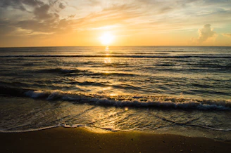 A serene beach at golden hour with gentle waves lapping the shore under a vibrant sunset sky.