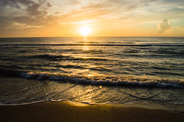 A serene beach at golden hour with gentle waves lapping the shore under a vibrant sunset sky.