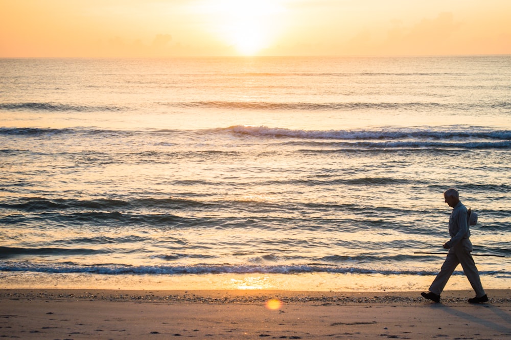 man walking beside ocean at sunset